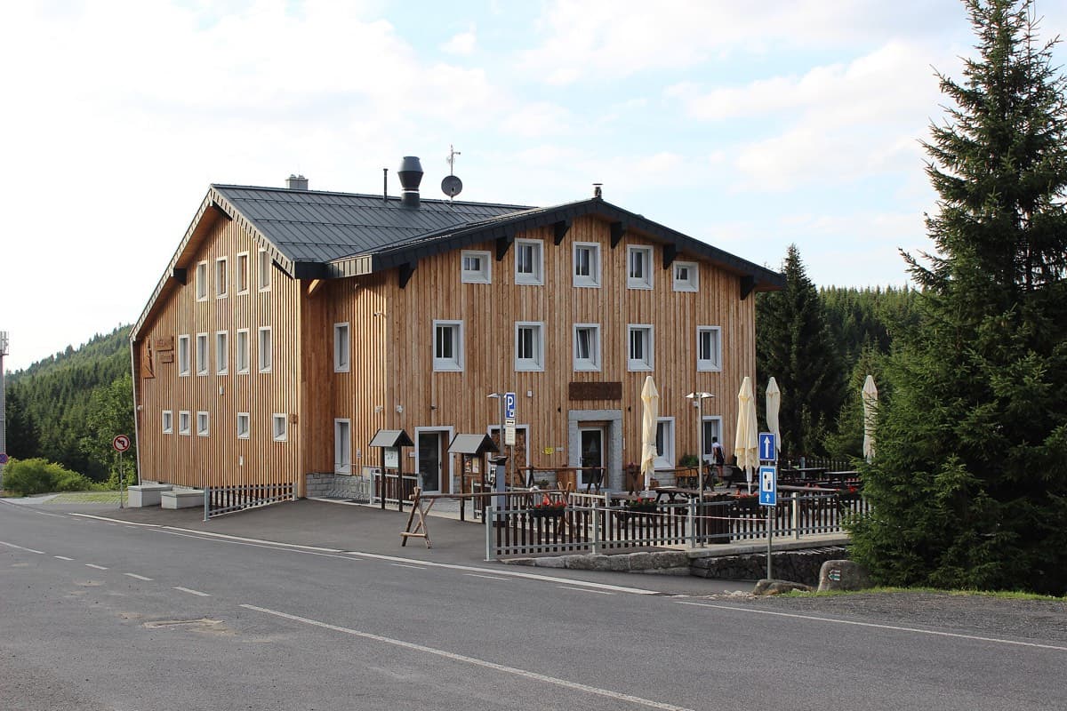 Světlá horská chata s dřevěnými balkony a terasou před vchodem